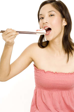 A pretty young asian woman eating sushi using chopsticksの写真素材