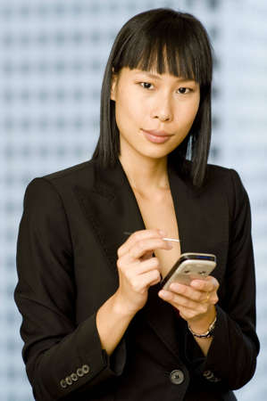 A young asian businesswoman using a personal digital assistant with building in background (shallow depth of field used)の写真素材