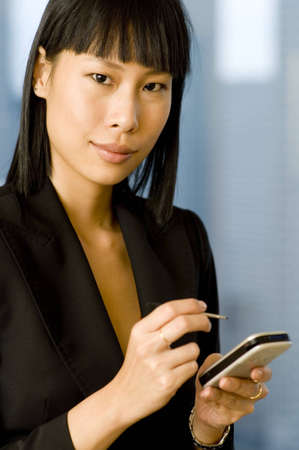 A beautiful asian businesswoman holding a smartphone with stylus (shallow depth of field used)の写真素材