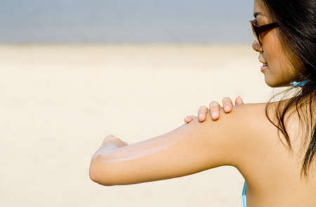 A young Asian woman applying suncream at the beach on sunny dayの写真素材