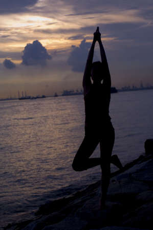 A young woman doing a yoga pose by the sea at sunsetの写真素材