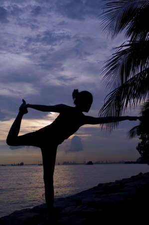 A young woman doing a yoga pose by the sea at sunsetの写真素材