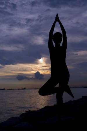 A young woman doing a yoga pose by the sea at sunsetの写真素材