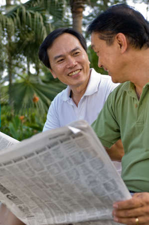 Two Chinese men in their fifties reading the newspaper in the parkの写真素材