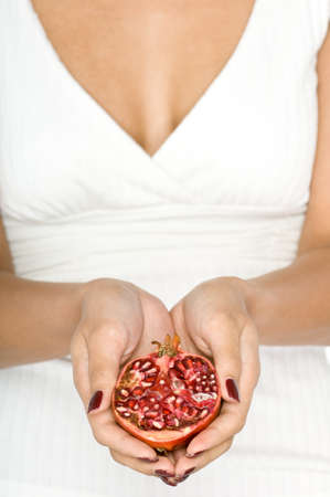 A young attractive Asian model holding half a  whole pomegranate on white backgroundの写真素材