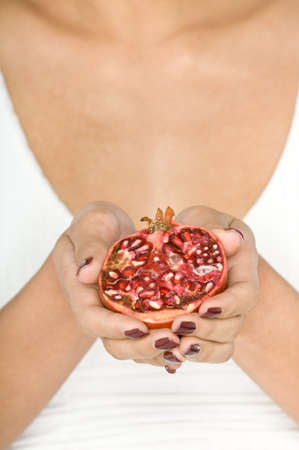 A young attractive Asian model holding half a  whole pomegranate on white backgroundの写真素材