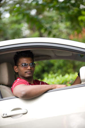 A good-looking Indian man in sunglasses sitting in drivers seat of car outside