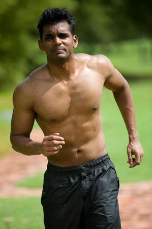 A young man with no top on running outsideの写真素材