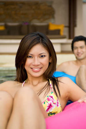 A young couple sitting in rubber rings in swimming poolの写真素材