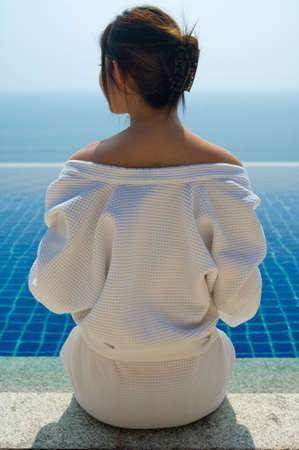 A young woman in a robe looking at her pool and sea viewの写真素材