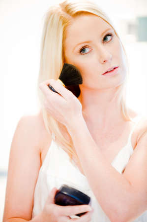 A young attractive woman in bathroom applying powder to her faceの写真素材