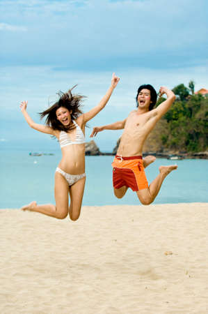 Two young adults jumping in the air on the beachの写真素材