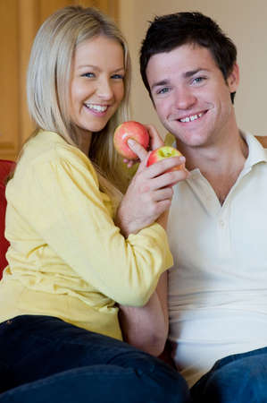 A young couple at home on the sofa with applesの写真素材