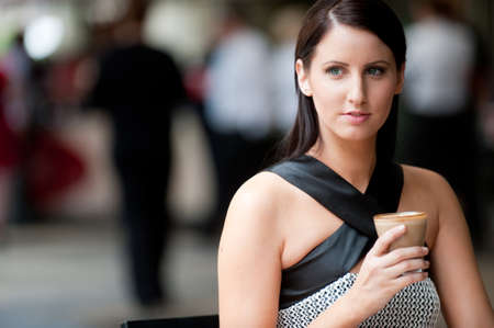 A stylish young woman sitting at a cafe with coffee (people behind out of focus)の写真素材