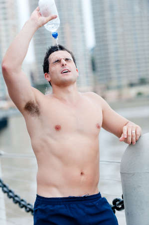 A man squirts water over himself after exercisingの写真素材
