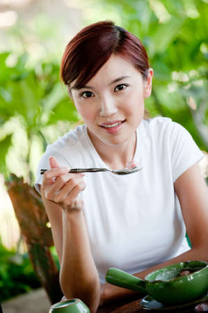 A young attractive Chinese woman eating fruit and yoghurt for breakfast at a tropical resortの写真素材