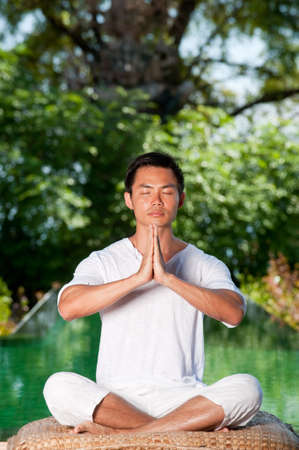 A young Chinese man meditating outside with trees and pool behindの写真素材