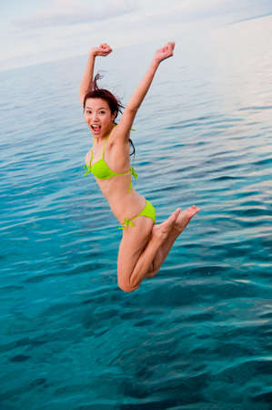 An attractive Chinese woman jumping into the seaの写真素材