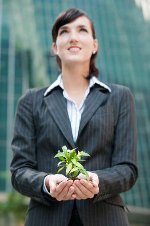 An attractive businesswoman cupping a plant in her hands against city backdropの写真素材