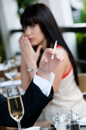 A young and attractive woman covers her nose to avoid the smoke from a cigarette at an outdoor dining areaの写真素材