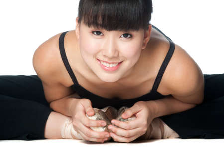 A young asian ballerina doing stretches and warm ups against white backgroundの写真素材