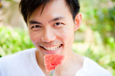 An attractive asian man eating a watermelon outdoorsの写真素材