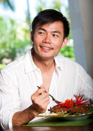An attractive asian man eating at a restaurantの写真素材
