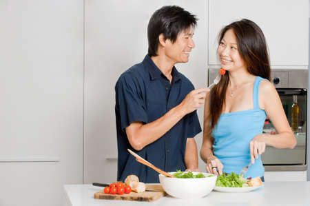 A good looking couple preparing a meal of bread and salad in the kitchen at homeの写真素材