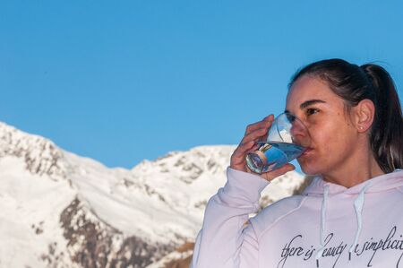 woman drinks a glass of pure mountain water, mountains background and blue sky