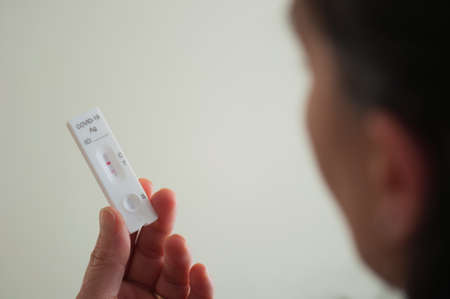 a blurred woman's face shows a positive rapid covid-19 test