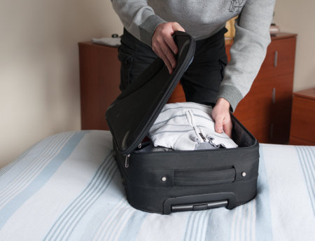 man prepares suitcase leaning on the bedの写真素材