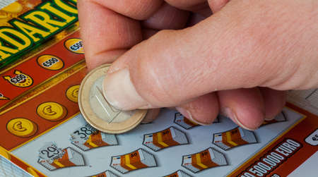 hand of a woman scratching an instant lottery ticket with a one euro coin