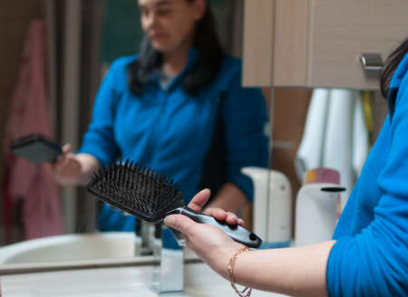 woman looks at hair brush with lost hair on it. hairbrush in foreground, woman blurred in background