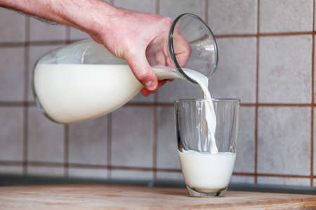 a man's hand holds a jug and pours milk into a glassの写真素材