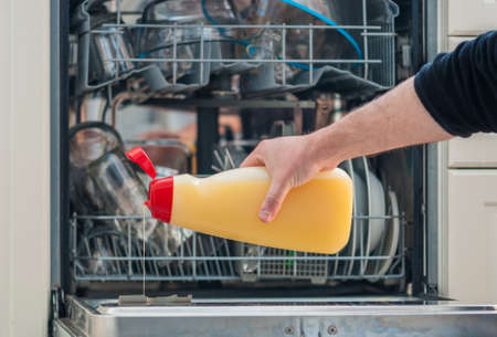 arm of a man holding a bottle of detergent and pouring it into the dishwasherの写真素材