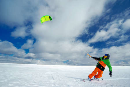 Male Athlete rides in the winter snowboarding and controls the kite. A clear winter day with clouds. Performs stunts and jumpsの写真素材