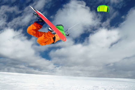 Male Athlete rides in the winter snowboarding and controls the kite. A clear winter day with clouds. Performs stunts and jumpsの写真素材