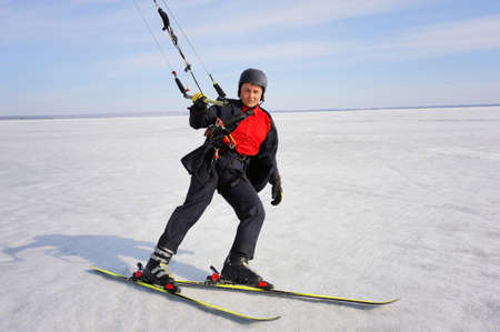 Male businessman in a classic suit. Skiing and controls the kite. Winter day and clean blue skyの写真素材