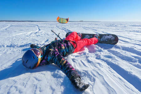 snowboard and people in bright clothes lying in the snow on a snowboard and kite controls. Deep blue sky and sun in the backgroundの写真素材