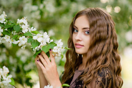 woman in an evening dress for a walk in the park in the spring. Posing on a background of flowering trees in the park. Spring blooming apple and cherryの写真素材