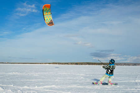 Beautiful young woman is kiting on the background of snow and blue sky at sunny dayの写真素材