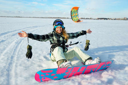 Beautiful girl is siting on the snow with kite on her legs on the background of snow and blue skyの写真素材