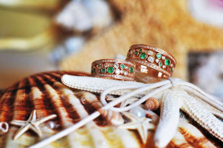 Vintage wedding rings of gold, diamonds and emeralds. Lie on the scenery of starfish and seashells