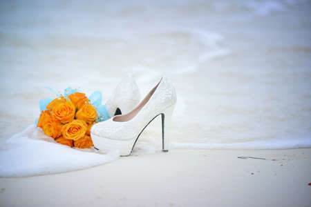 The bride's bouquet and shoes are on the beach in the sea foamの写真素材