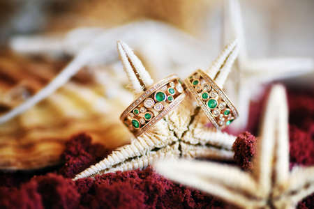 Wedding rings with diamonds and emeralds are lying on the sea star.の写真素材