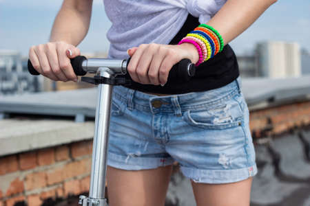 Close-up horizontal view young woman in shorts is holding her hands with bright colorful bracelets...