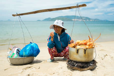 NHA TRANG, VIETNAM - JUNE 19, 2016: Merchant is selling lobsters to tourists on a beach on background of the sea and mountains in Vietnamのeditorial素材