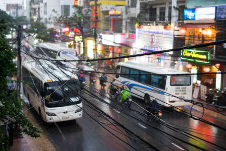 NHA TRANG, VIETNAM - JUNE 20, 2016: Evening view of the downtown with illuminated signs on the shops and busses, motorbikes and bycicles on the traffic road at rainy weatherのeditorial素材