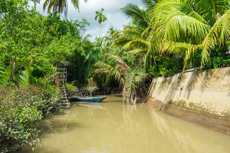 HO CHI MINH CITY, VIETNAM - JUNE 26, 2016: Empty tourist boat is parked near the coastline of  the tropical river with muddy water on a mooring at vietnamese village. View to the jungle at summer sunny dayのeditorial素材