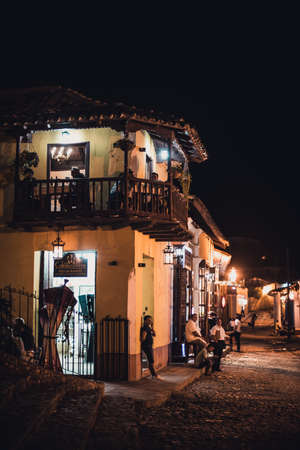 TRINIDAD, CUBA - FEBRUARY 25, 2014: View to local two-storeyed house restaurant with balcony and illumination inside. Tourists are eating there and walking on a central street at summer night.のeditorial素材